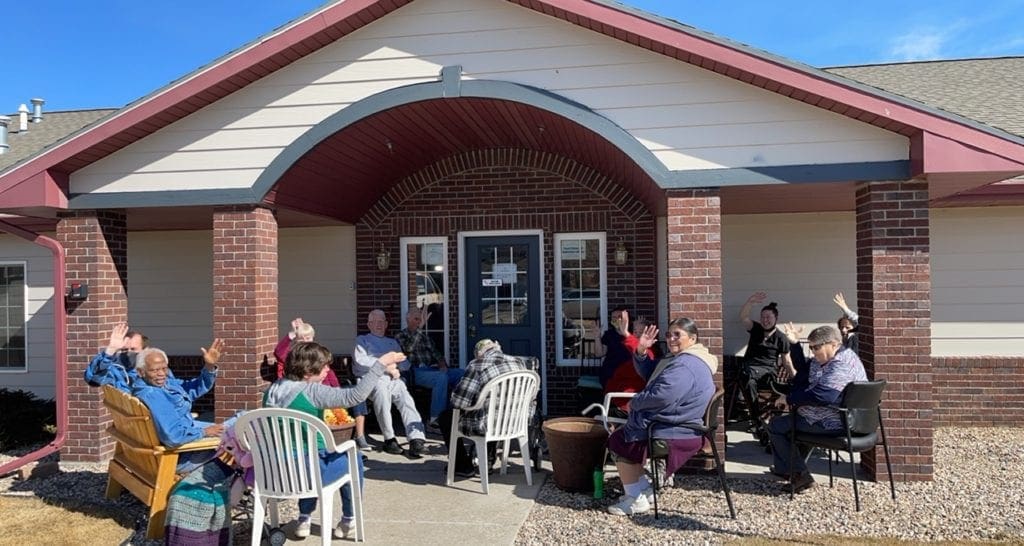 group of seniors sitting on patio waving at camera
